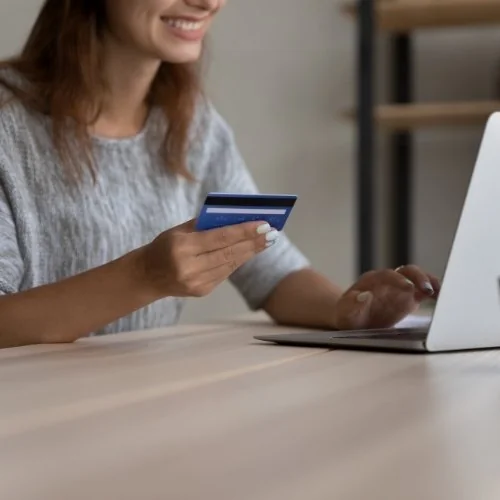 Une femme tient une carte bancaire devant un ordinateur portable.