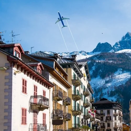 Un avion dans le ciel au-dessus d’un village et de montagnes enneigées.